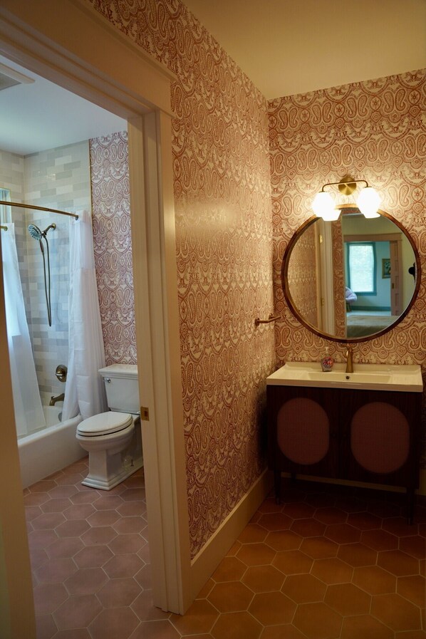 Un baño con inodoro, ducha, tocador con espejo y papel tapiz estampado.