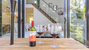 Une bouteille de vin Frontera Cabernet Sauvignon et deux verres à vin sont posés sur une table en bois, offrant une vue sur un intérieur moderne comprenant un escalier et un canapé.