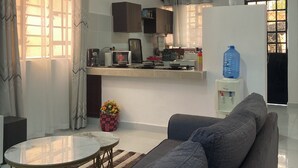 Una sala de estar moderna con un sofá gris, una mesa de centro de vidrio y un comedor, con una cocina al fondo.