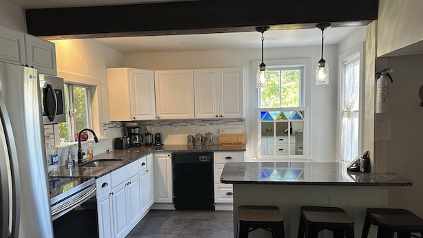 A kitchen with white cabinets, a dishwasher, a refrigerator, a coffee maker, and a window with a view of greenery. - Soothing getaway farmhouse in Leeds near Hudson, Grace’s cafe, the creek, HITS. (Catskill)