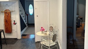 A dining area with a round table, metal chairs, and a small vase with flowers. A wooden door with a red handle and a white door with a stained glass window are visible. - Soothing getaway farmhouse in Leeds near Hudson, Grace’s cafe, the creek, HITS. (Catskill)