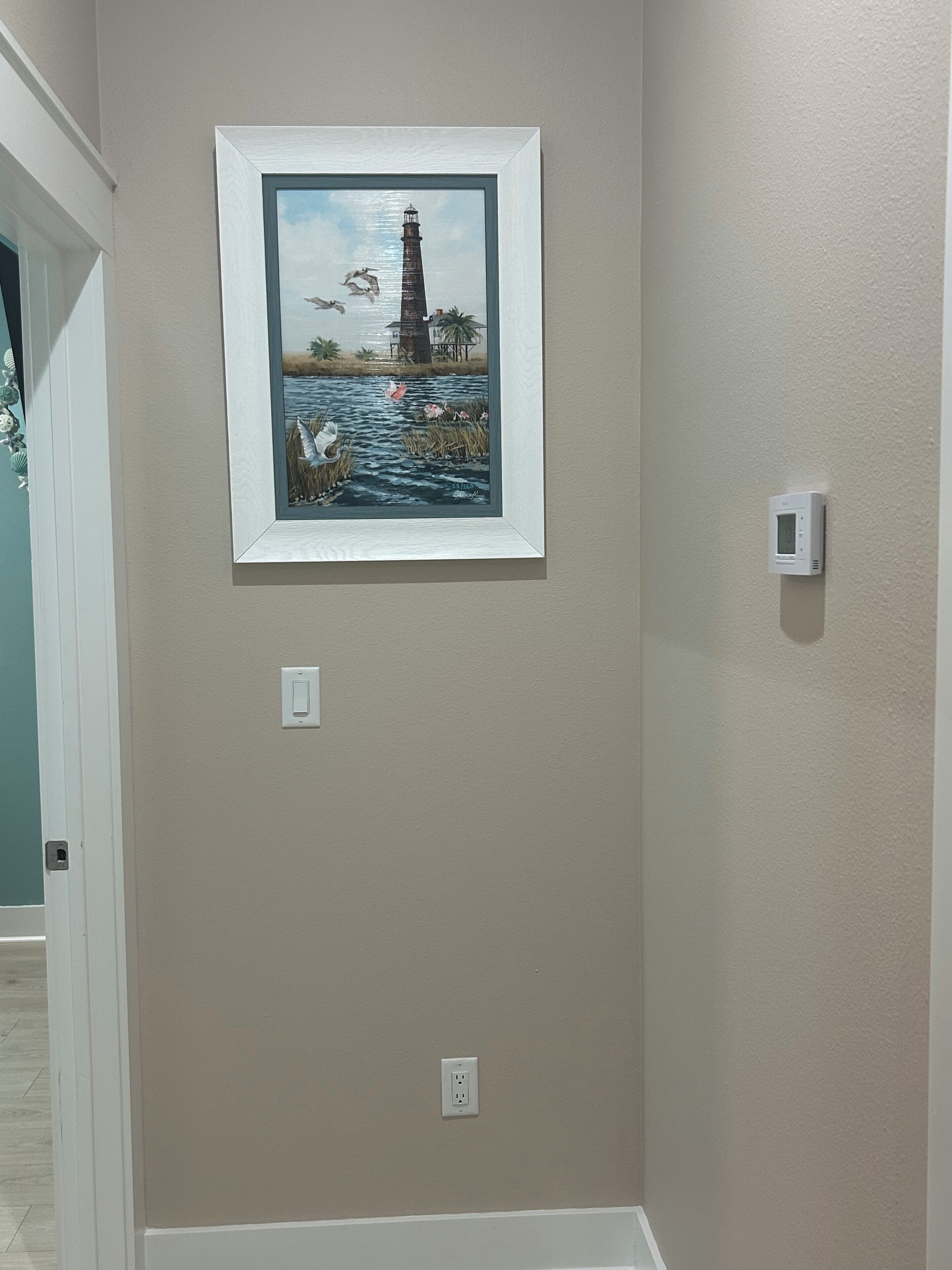 A framed painting of a lighthouse and seagulls on a wall.