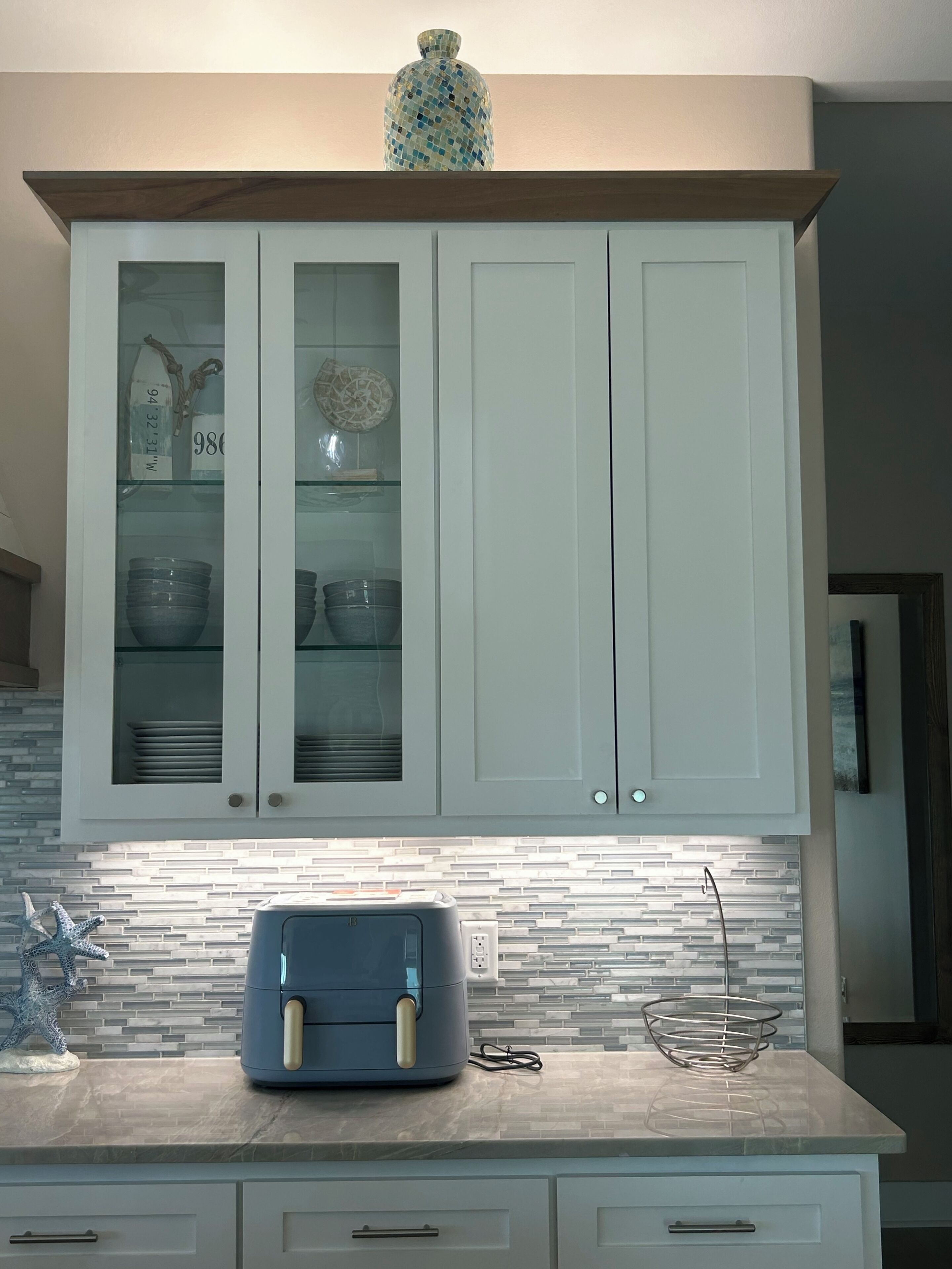 A kitchen with white cabinets, a toaster on the counter, and a decorative vase on the shelf.