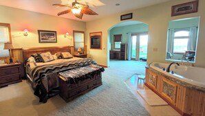 A bedroom with a large bed, a ceiling fan, a bathroom with a bathtub, and a view of the outdoors. - Cozy up on Lake Osakis (Osakis)