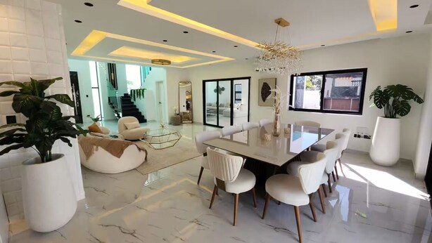 Un comedor moderno con suelo de mármol, mobiliario blanco y amplias ventanas que dejan entrar luz natural.