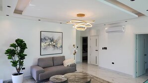 Una sala de estar moderna con un sofá gris, un cuadro abstracto grande, una planta en maceta y una lámpara de techo original.