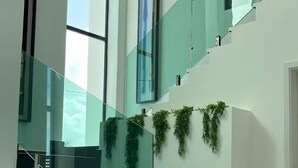 Una escalera moderna con barandillas de vidrio y plantas, que conduce a un segundo piso.