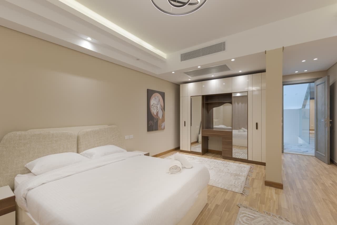 A modern bedroom with a large bed, a walk-in closet, and a sliding glass door to the balcony.