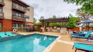 Ein Schwimmbad mit Liegestühlen, einem Grillbereich und einer überdachten Terrasse.