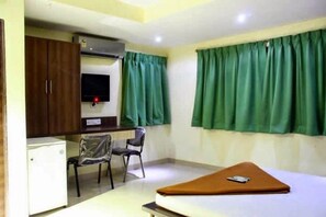 Une petite pièce comprenant un lit, un bureau, une chaise, un téléviseur et une fenêtre avec des rideaux verts.