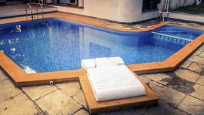 A rectangular swimming pool with a wooden deck and a white lounge chair with a towel. - Hotel Samudra City (Alibag)