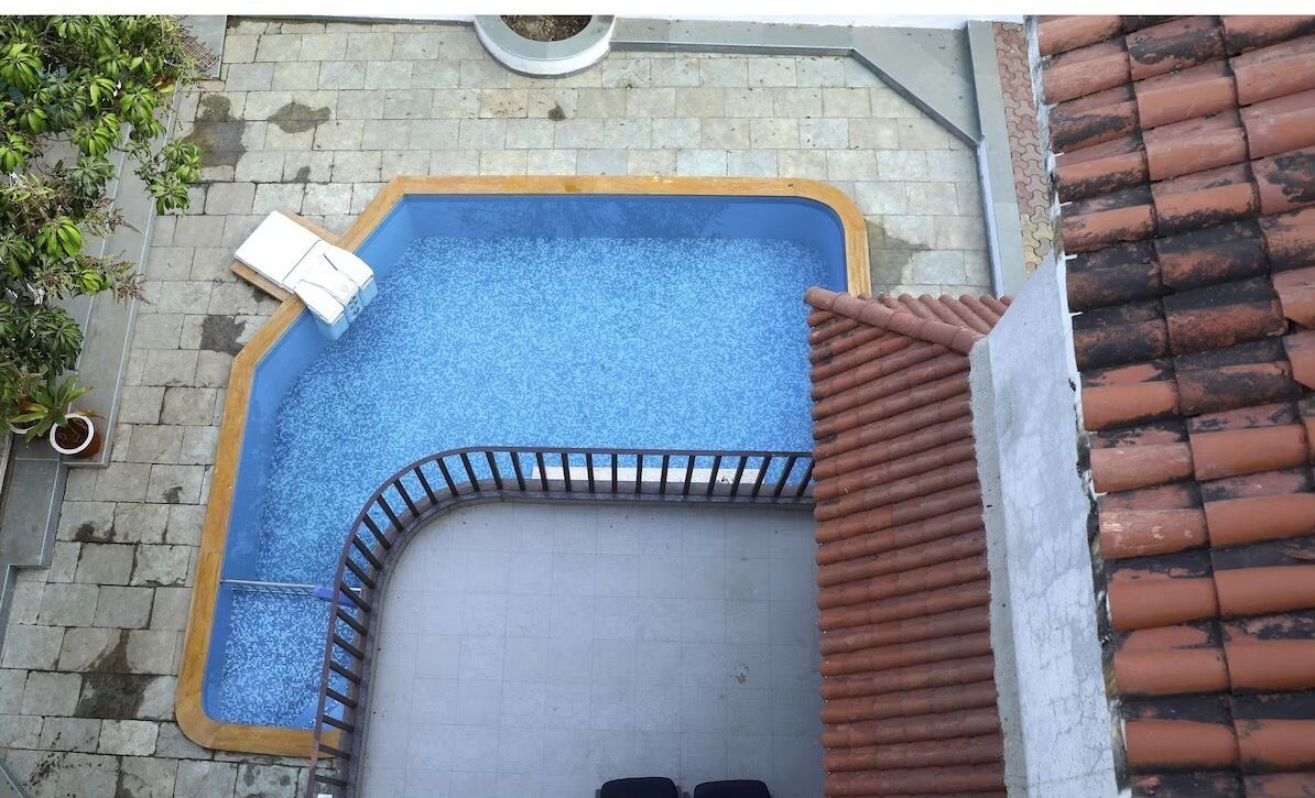 A rectangular swimming pool with a blue interior, surrounded by a brick wall and a tiled roof.