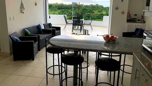 A modern kitchen with a bar area, dining table, and chairs. There is a view of greenery through the windows. - Vacation, Apartment at the Beach Club Casa Blanca, Same, Ecuador (Same)