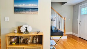 Een houten console tafel met decoratieve objecten, een rieten speaker en daarboven een schilderij van een strandgezicht.