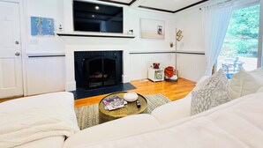 Een woonkamer met een open haard, witte muren en een groot raam.