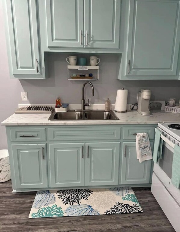 A kitchen with teal cabinets, a double sink, a stove, and a patterned rug. - BB On The Bayou (Gautier)