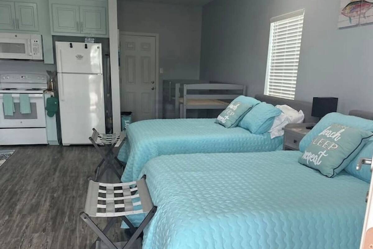 Ein kleines Zimmer mit zwei Betten, einer Küchenzeile und einem Deckenventilator.