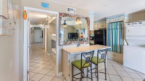 Una cocina compacta con una isla central, dos sillas con cojines verdes, un refrigerador y una cortina a rayas.