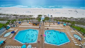 Un resort frente a la playa con dos piscinas grandes, tumbonas y vistas al océano.