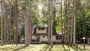 A cabin surrounded by tall trees, with a porch and a small deck.