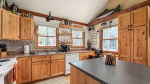 A kitchen with wooden cabinets, a stone backsplash, a sink, a stove, and a countertop with various kitchen items.