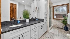 A bathroom with a large mirror, white cabinets, a sink, and a potted plant.