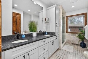 A bathroom with a large mirror, white cabinets, a sink, and a potted plant.