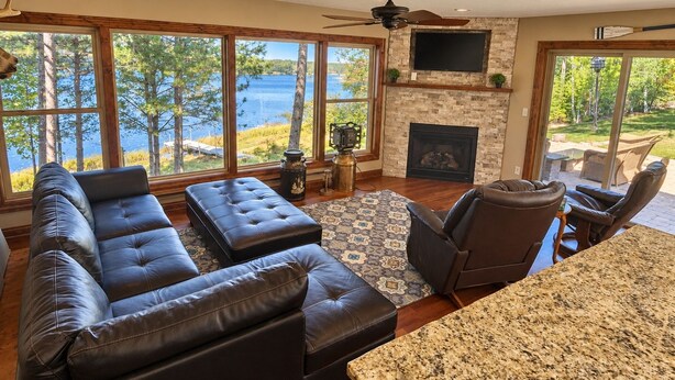A spacious living room with a large window overlooking a lake, a fireplace, and a ceiling fan.