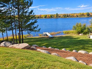A lakeside property with a dock, grassy areas, and a forest in the background.