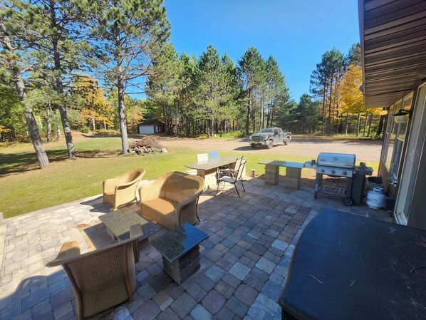 An outdoor patio with wicker furniture, a barbecue grill, and a truck parked in the background. - Lily Bay Lodge (Mercer)