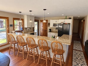 A kitchen with a central island, wooden chairs, pendant lights, and a refrigerator.