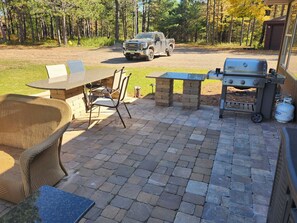An outdoor patio with a grill, seating, and a truck in the background. - Lily Bay Lodge (Mercer)