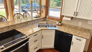 A kitchen with granite countertops, white cabinetry, a built-in dishwasher, and a stove.