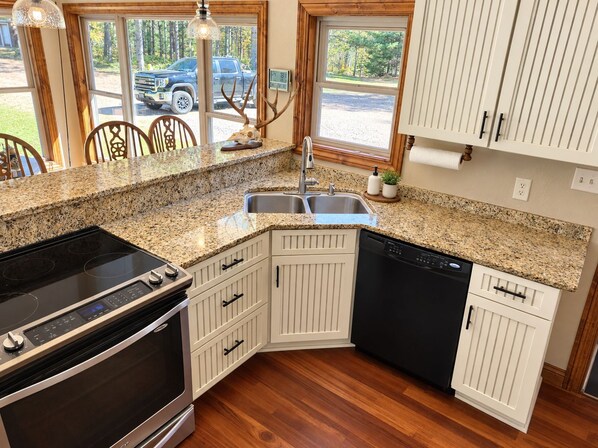 A kitchen with granite countertops, white cabinetry, a built-in dishwasher, and a stove.