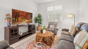 A living room with a flat-screen TV, a sofa, a coffee table, and a large painting.