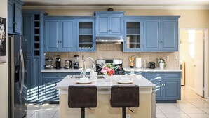 A kitchen with blue cabinets, a central island with two chairs, a refrigerator, and various appliances.