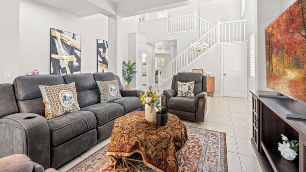 A modern living room with a sofa, armchair, and coffee table, a staircase, and a painting on the wall.