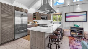 Une cuisine moderne dotée d’un grand îlot central, d’appareils électroménagers en acier inoxydable et d’un plafond haut avec des puits de lumière.