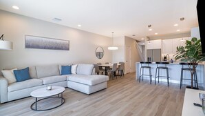 A modern living room with a sectional sofa, a round coffee table, and a dining area with a table and chairs.