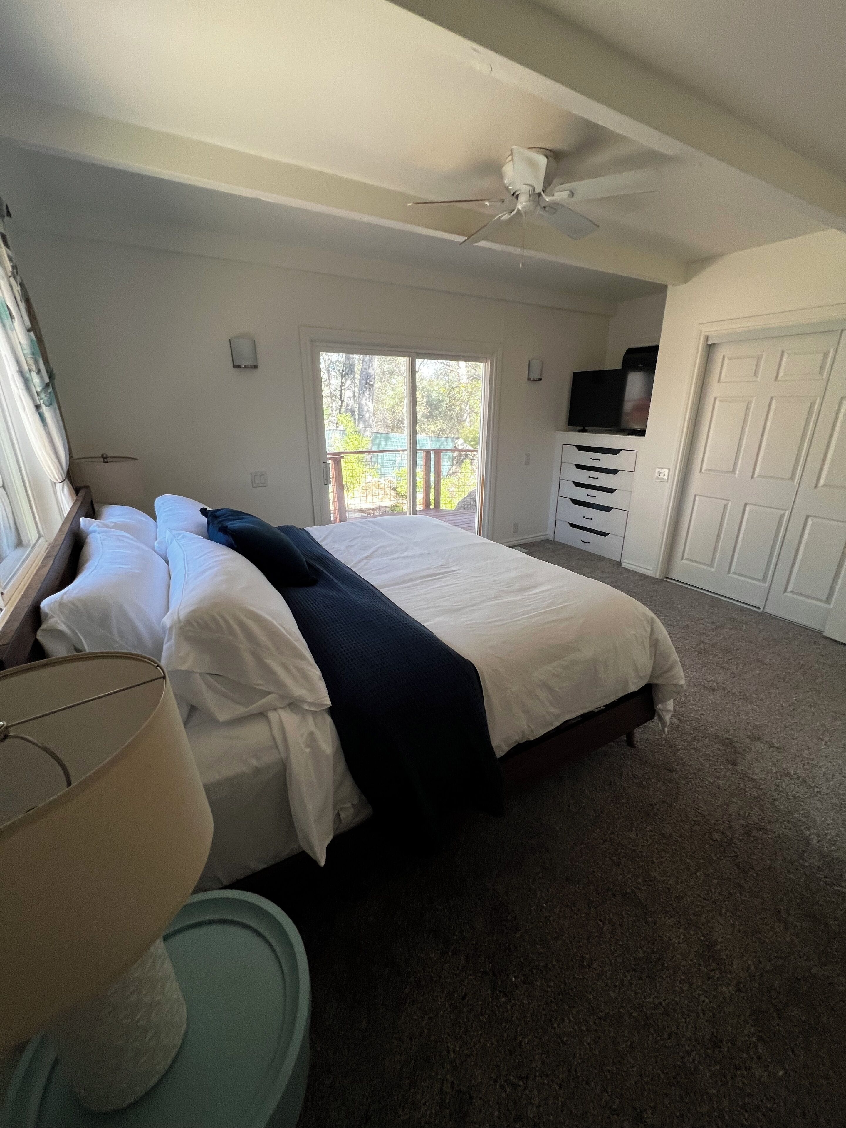 A bedroom with a bed, a dresser, a ceiling fan, a window, and a door.