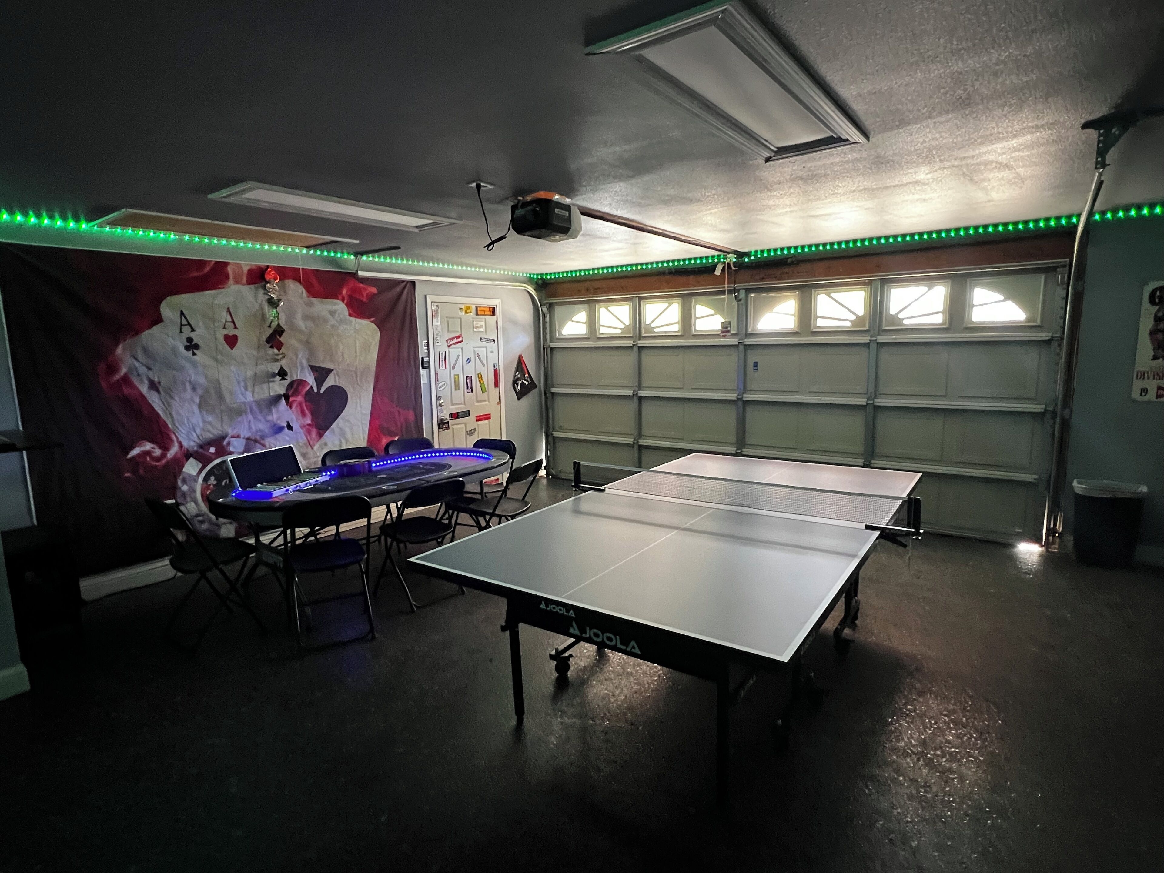 Una stanza con un tavolo da ping pong, sedie, un proiettore e un muro con un grande poster.