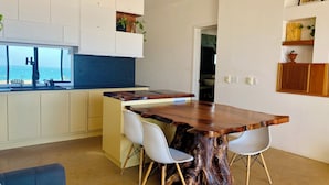 Una cucina moderna con isola in legno, sedie bianche e vista sul mare.