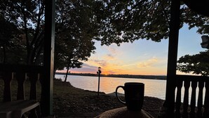 Vista desde un porche sobre un lago al atardecer, con una taza en un banco.