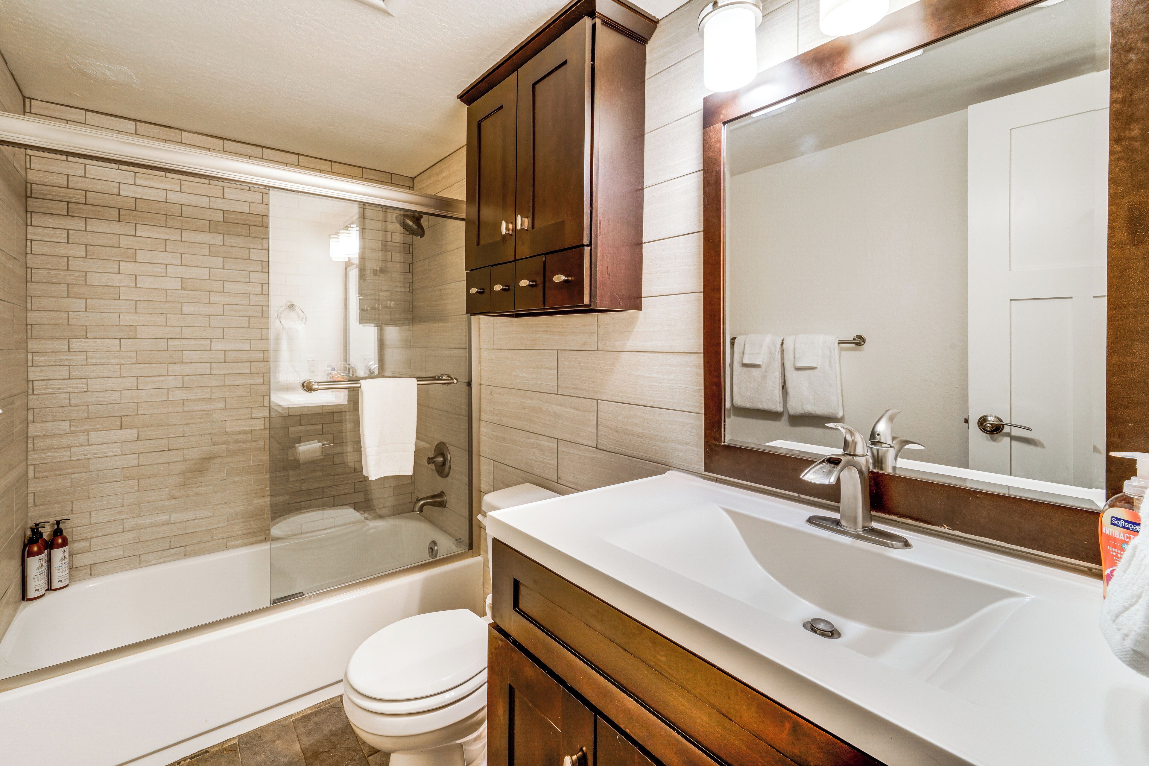 A modern bathroom with a glass-enclosed shower, a white toilet, and a vanity with a large mirror.