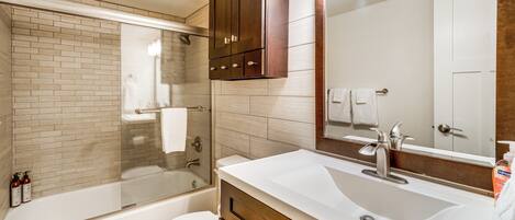 Une salle de bain moderne avec une douche à parois de verre, des toilettes blanches et un meuble-lavabo doté d’un grand miroir.