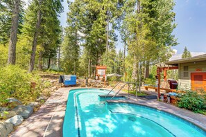A swimming pool with a wooden deck, surrounded by tall trees and a small building with outdoor seating. - Northstar Ski-in/out Condo w/ Resort Amenities! (Truckee)