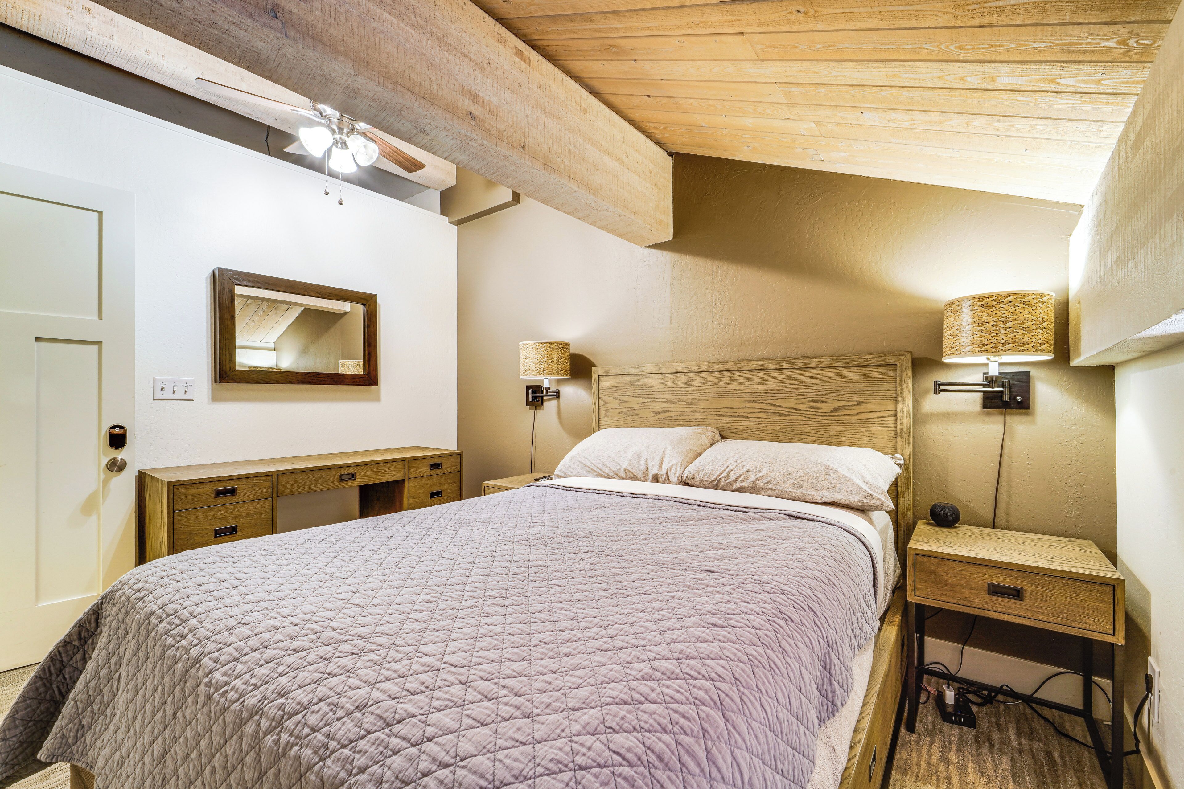 Ein Schlafzimmer mit Bett, Holz-Kopfteil, Nachttischlampen, einem Nachttisch und einem Deckenventilator.