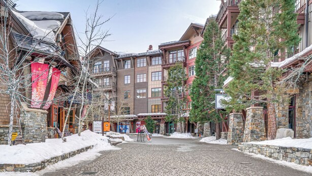 A snow-covered cobblestone street lined with multi-story buildings featuring stone facades and large windows. - Northstar Ski-in/out Condo w/ Resort Amenities! (Truckee)