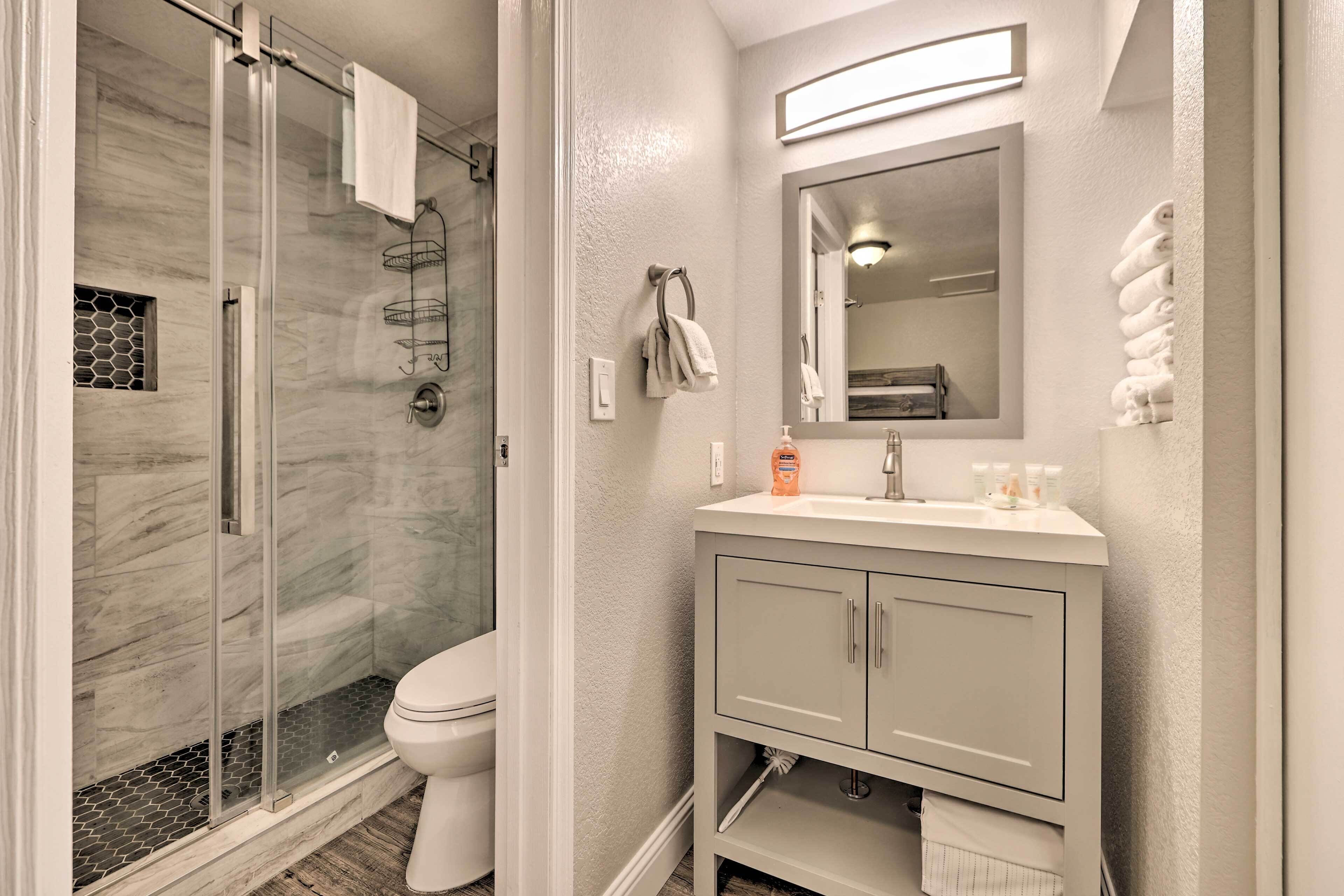 Un baño con cabina de ducha de vidrio, inodoro, tocador con espejo y toallas ordenadas.