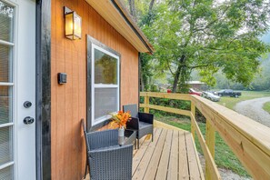 A wooden deck with wicker chairs and a vase of flowers, a wooden railing, and a view of a forested area. - Hudsons Hideaway Cabin on Creek in Beattyville! (Beattyville)